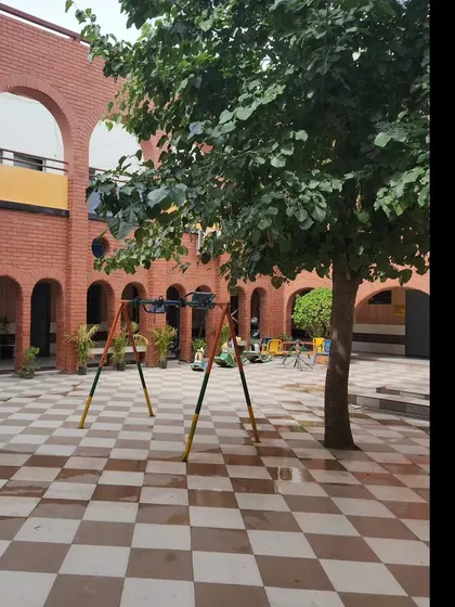 The school courtyard with its central tree and play equipment, showcasing its function as a green lung and recreational heart of the school. The design ensures a safe and engaging outdoor space for students.