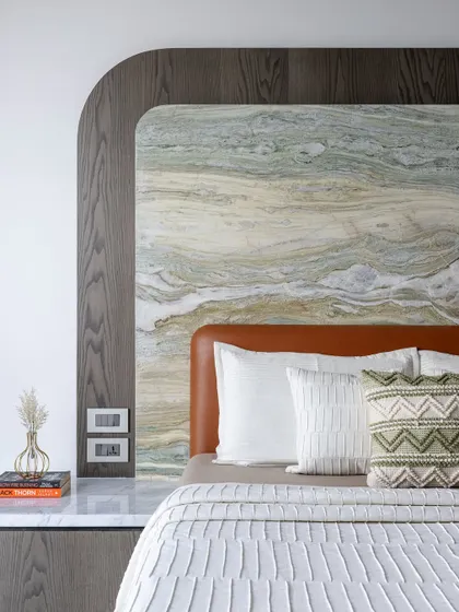 A close-up of the layered textures in the bedroom, with a rough stone slab, a dark wood frame, and a soft leather headboard.