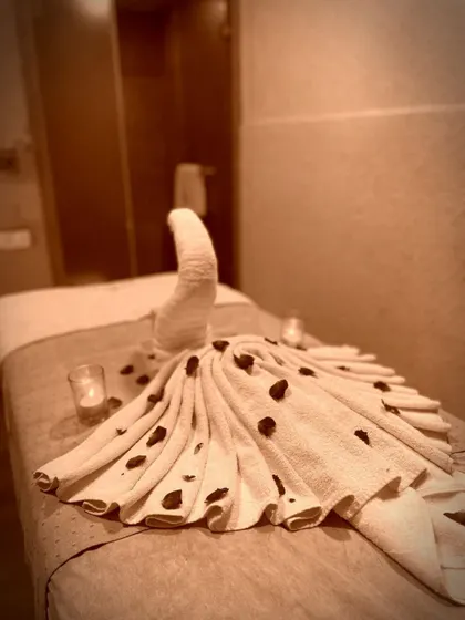 A close-up of the thoughtful details that await you. A towel folded into an elegant peacock design, scattered with petals, shows the care we put into making every moment of your visit special.
