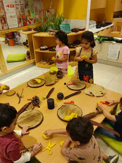 A table full of children engaged with playdough and loose parts. This communal setting encourages social interaction, language development, and collaborative creativity, all centered around a shared sensory experience.