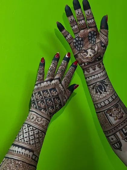 A full-arm bridal design with a variety of symbols, including a portrait, swastikas, and elephants, against a vibrant green background.