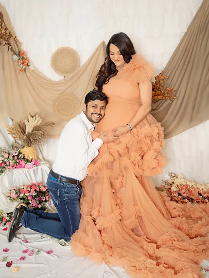 A classic pose filled with adoration. The dad-to-be kneels to connect with the baby bump, looking up at his smiling partner.