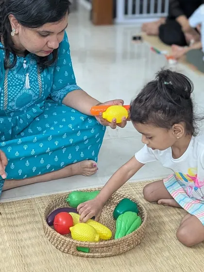 A mother helps her daughter identify different vegetables. These early interactions with our materials are unhurried, allowing the child to learn at her own pace with the comfort of a parent's presence.