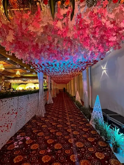 A magical indoor walkway with a ceiling covered in pink and red leaves. The lighting from below creates a beautiful, colorful glow, leading guests to the main reception area.
