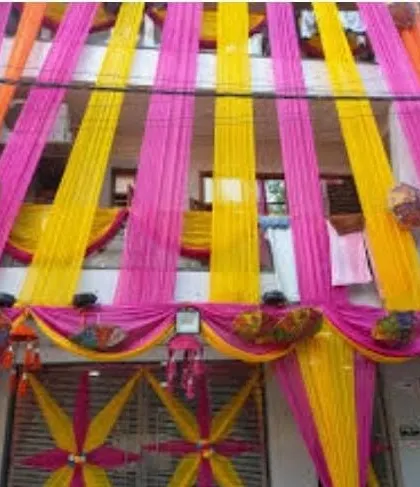 A house facade fully covered in vertical pink and yellow drapes, with a decorated gate and hanging umbrellas.
