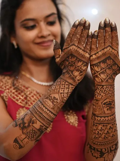 A happy client showing off her full-arm bridal mehendi, filled with intricate patterns.