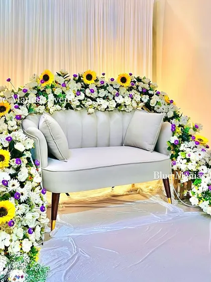 A unique floral couch decoration designed for a Roka ceremony. This statement piece wraps the seating in a cascade of sunflowers and white daisies, creating an unforgettable focal point for your event.