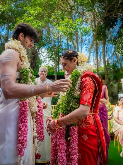 A smiling couple during their garland exchange ceremony, surrounded by lush greenery and their closest family. These are the happy, traditional moments I love to create.