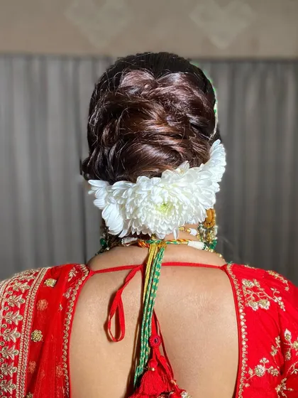 A classic bridal updo with a large bunch of white chrysanthemums. This is a bold and beautiful choice that pairs wonderfully with a traditional red lehenga.