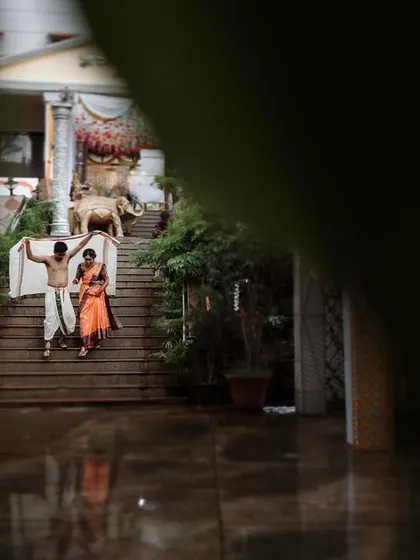 A wide shot of a couple walking down the steps of a traditional venue, framed by foliage. This image captures both the couple and the beautiful architecture of their wedding location.