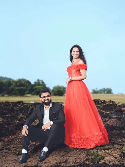 A relaxed moment during their outdoor pre-wedding shoot. The red rose gown adds a touch of elegance and romance to the rustic setting.