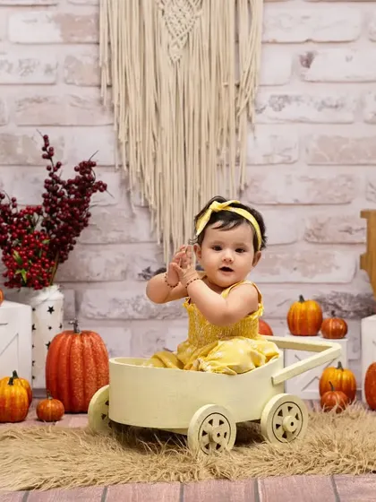 A happy harvest day at our pumpkin farm. This little girl in her bright yellow dress is all smiles while sitting in a rustic wagon, part of our detailed autumn-themed setup.