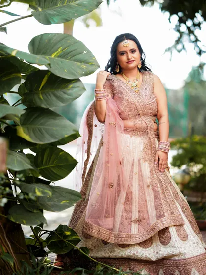 An elegant bridal portrait in a garden setting, showcasing a beautiful pink and white lehenga.