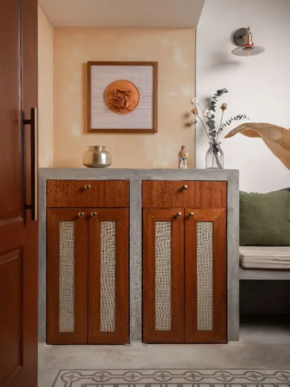 The foyer features a custom-designed shoe cabinet with rattan-paneled doors, set within a concrete-finished base. This unit provides practical storage at the entrance.