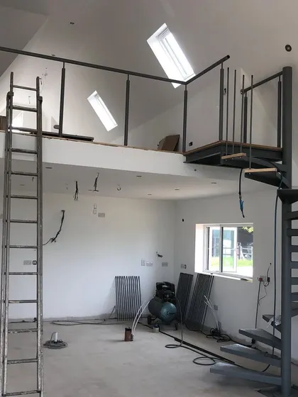 The steel frame of the spiral staircase and mezzanine railing installed on site, before the wooden treads and other finishes are added.