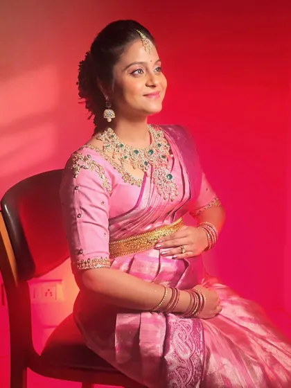 A beautiful seated portrait of Chandralekha, cradling her baby bump. Her makeup features a pop of pink on the eyes.