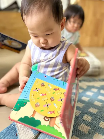A baby explores a lift-the-flap book, a fun and interactive way to engage with stories and develop fine motor skills.