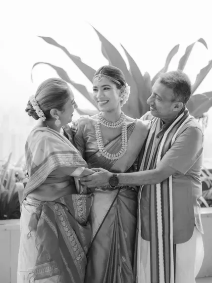 A heartwarming black and white photo of the bride sharing a loving moment with her parents, their hands clasped together.