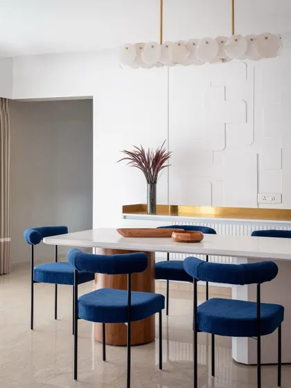 We love adding a pop of color to create drama and personality. In our 'Vishu Home' project, these bold, royal blue velvet chairs stand out against the monolithic white dining table and textured wall, creating a modern yet timeless dining experience that is both elegant and inviting.