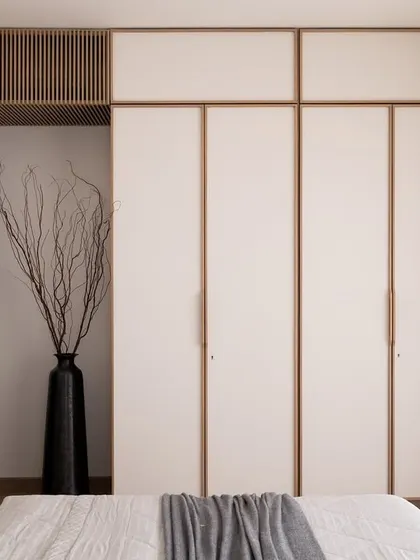 This view of the master bedroom showcases the custom white wardrobes with wood trim. The design maintains a clean, uncluttered look while providing ample storage, contributing to the room's serene atmosphere.