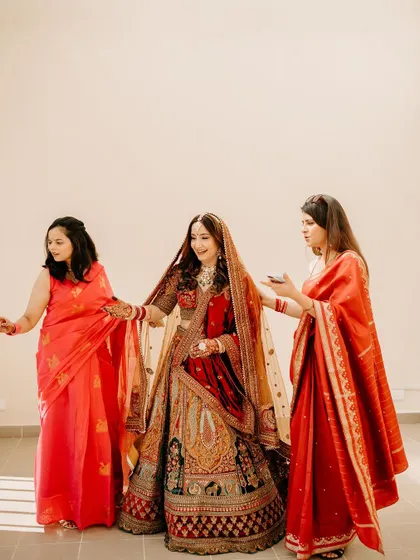 The bride stands with her bridesmaids, all dressed in shades of red and pink, a beautiful group portrait.