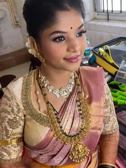 A beautiful post-wedding reception look for Gagana. The makeup features soft pink eyeshadow and a matching lip, complementing her pastel pink and gold Kanjivaram saree.