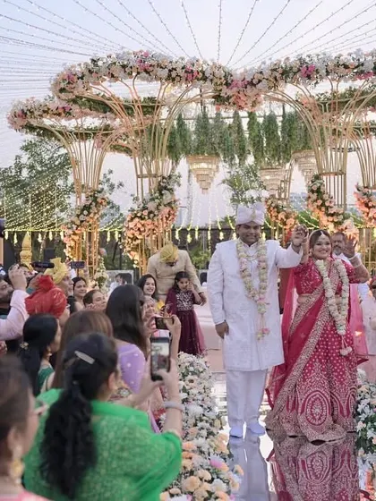 The couple's grand entrance down the mirrored aisle, surrounded by guests, with the stunning floral mandap as their destination.