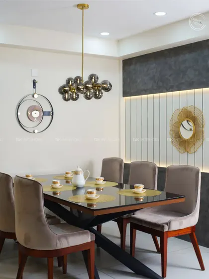 This elegant dining room uses a neutral color palette with grey upholstered chairs and a glass-top table. The feature wall with white reapers and a decorative mirror adds texture and interest.