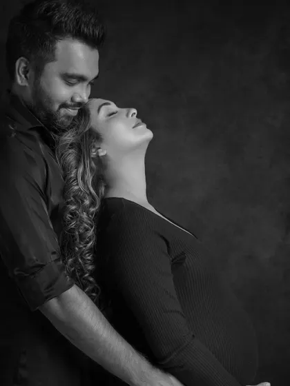 A moment of pure bliss. The mother-to-be leans her head back in peaceful joy as her partner embraces her from behind, captured in a stunning black and white profile.