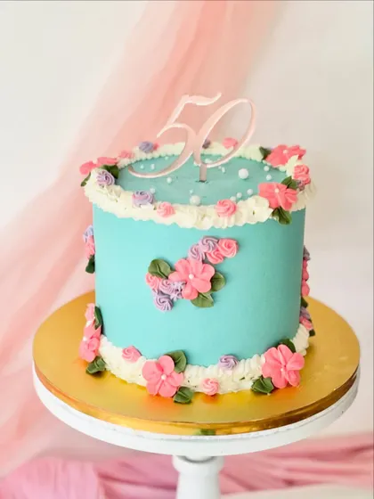 A pretty turquoise cake for a 50th birthday. The cake is decorated with clusters of small, hand-piped pink flowers and a clear acrylic topper.