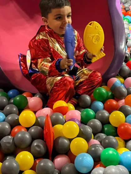 A boy in a shiny costume plays with toys at the bottom of the slide in the ball pit. There's fun to be had in every corner.
