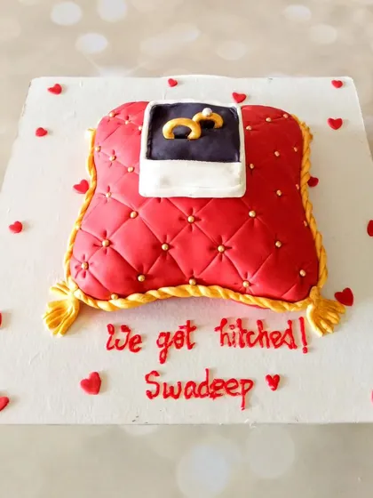 This engagement cake is designed to look like a ring cushion. The red fondant pillow is quilted and detailed, with the engagement rings presented in a box on top.
