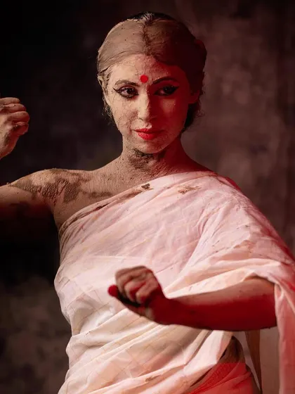 A powerful pose from the second phase of the photo story. The red-painted fingertips contrast with the earthy clay, signifying the emergence of the goddess's divine power and warrior aspect.