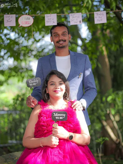 A fun and interactive baby shower photo idea. The couple holds "Mommy to be" and "Daddy to be" signs, with a cute banner of baby predictions in the background.