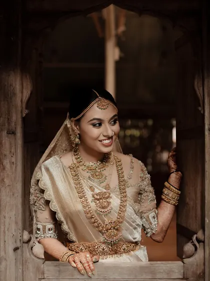 This bride looks like a painting in her off-white Kanchivaram saree. The custom blouse with sheer embroidered sleeves adds a touch of modern elegance to her traditional look.