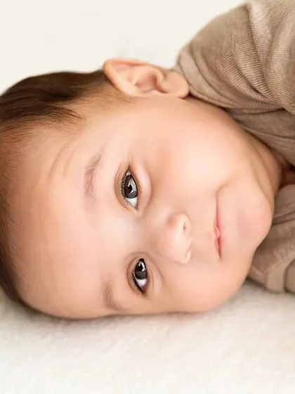 A baby boy lies on a simple white blanket, looking curiously at the camera.