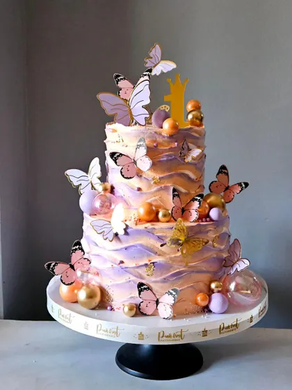 Butterflies and balloons celebrate a first birthday in pastel peach and lavender. This three-tier whipped cream cake has a beautiful textured finish.