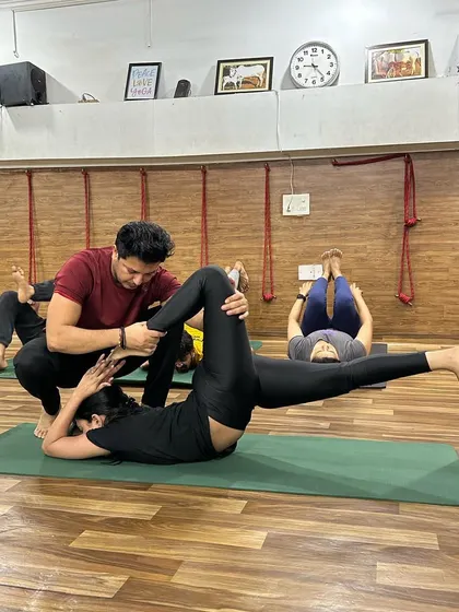 An instructor assists a student in a supine leg stretch, focusing on alignment and deepening the posture safely.