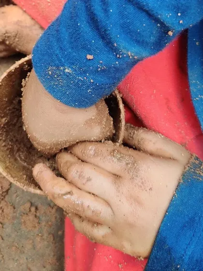 A child pats mud into a bowl, perhaps making a cake or a potion. In the world of play, the possibilities are endless.