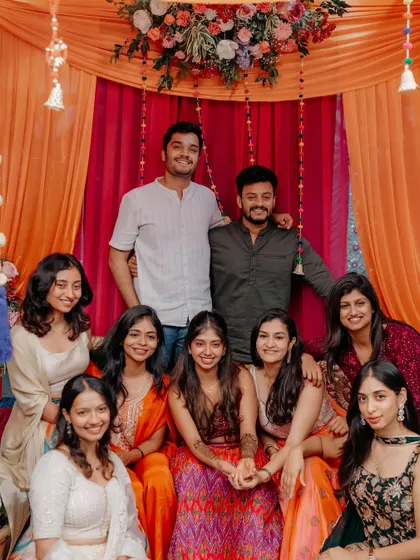 The bride and her friends pose for a group photo at a vibrant Mehendi, seated on a beautifully decorated swing.