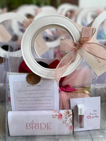 A close-up of a bridesmaid gift bag, showing a personalized note, custom-wrapped chocolate, lipstick, and other treats. The bag is finished with a personalized tag and a wax seal.