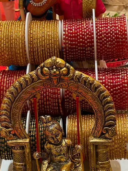 Another view of a bangle display for a traditional function. A small Krishna idol on a swing is placed inside a bowl, with bangle stands arranged behind it.