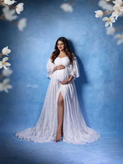 A serene portrait of the mom-to-be in her white gown, framed by beautiful white flowers against a sky-blue background.