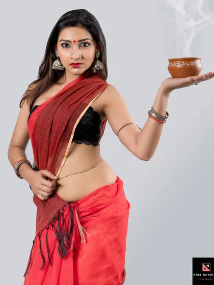 An ethereal portrait featuring a model in a red saree holding a steaming earthen bowl. The soft smoke and her intense gaze create a mystical and traditional atmosphere.