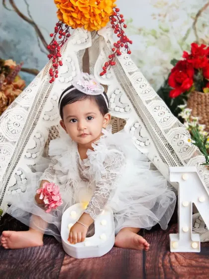 Her sweet, curious look is so precious. The combination of rustic wood, soft lace, and colorful flowers creates a beautiful setting for a one-year-old's photoshoot.