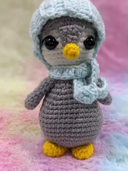 A full-body shot of the penguin amigurumi against a soft, colorful blanket.