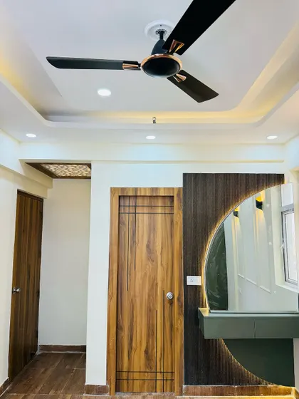 A bedroom design featuring a stylish dressing unit with a large, backlit arched mirror. The wooden door and false ceiling details add to the room's character.