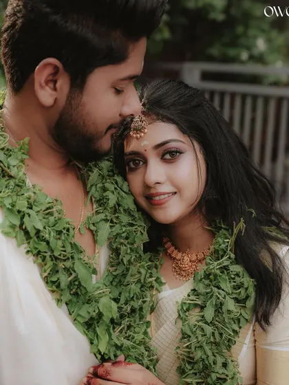 A tender moment with the groom kissing his bride's forehead, both adorned with traditional garlands.