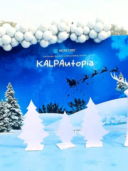 A wide view of the 'KALPAutopia' corporate winter festival setup, showcasing a large custom-printed backdrop with the company's branding. We flanked the scene with life-sized reindeer props and decorative trees to create an immersive experience.