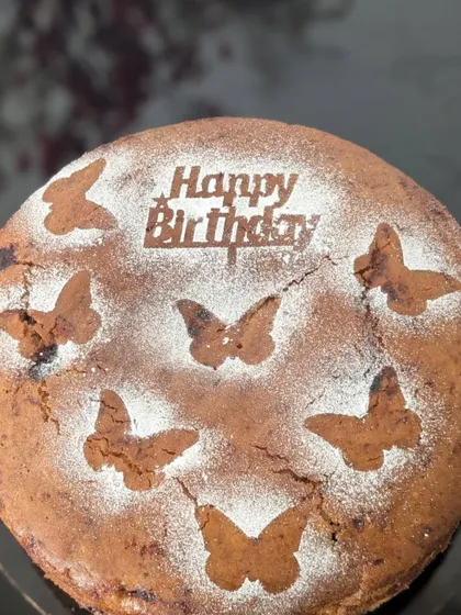 A popular choice for kids' birthdays, this atta jaggery cake is decorated with whimsical butterfly patterns using powdered sugar. It comes with a 'Happy Birthday' topper to complete the festive look, all without any heavy frosting.